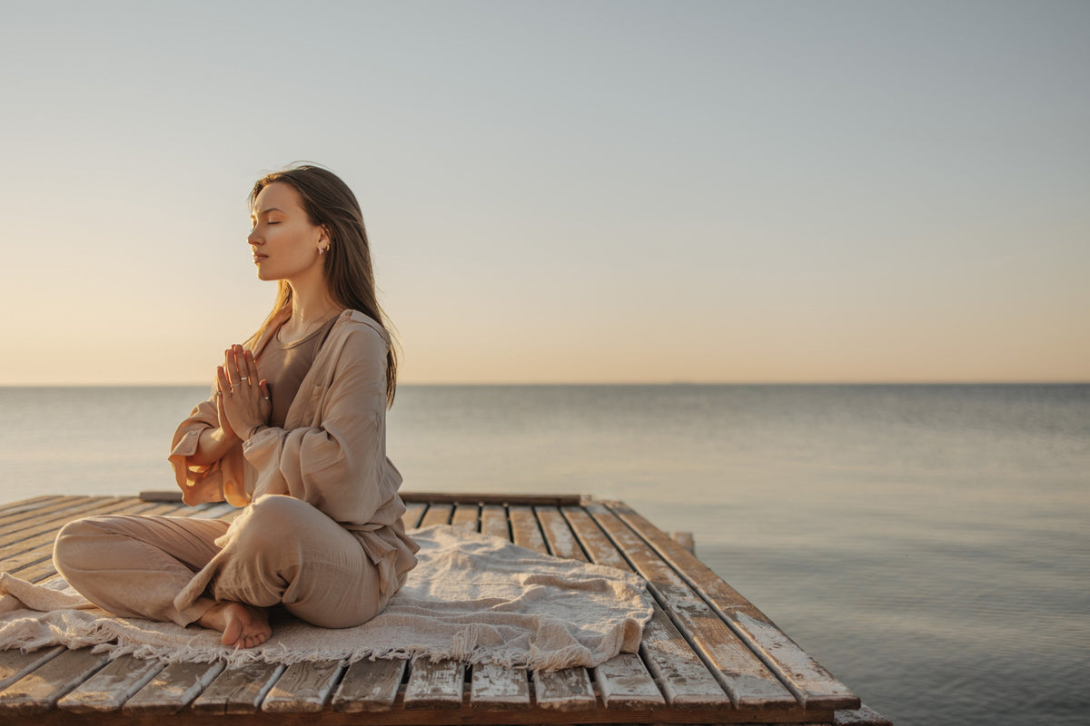Woman meditating peacefully beside calm water.